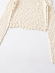Detail of off-white knit top featuring hollow-out patterns and unique wavy hemline