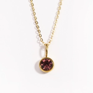 Detailed close-up of a gold necklace with a round pink-purple gemstone pendant