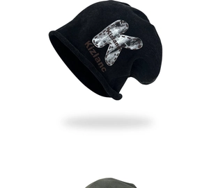 Detail of black knit beanie featuring large K letter print and silver rivet accents