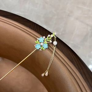 Detail of vintage gold hairpin with blue flowers, green leaves, and pearl tassels