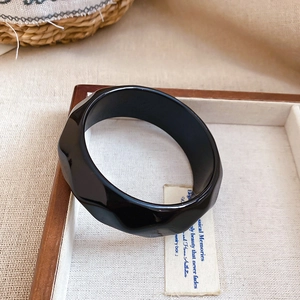 Macro shot of black geometric twisted acrylic bangle in a minimalist wooden display tray