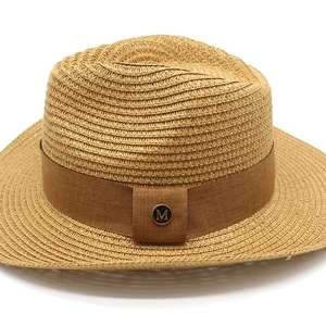 Dettaglio cappello di paglia con fascia marrone e stemma metallico dorato con lettera M