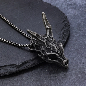 Vintage stainless steel dragon bone skull pendant on a textured stone surface