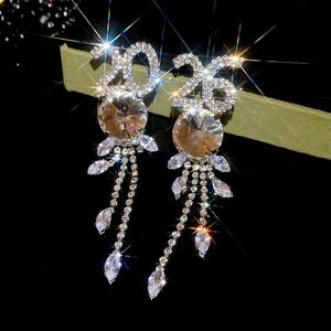 Détail de boucles d'oreilles argentées avec numéros 2025 et longs glands en strass