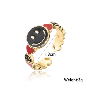 Close-up of gold-plated open ring with black smiley face and red heart enamel detail