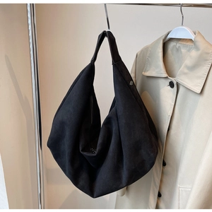 Detail of a large black suede hobo bag hanging on a stand with a beige trench coat