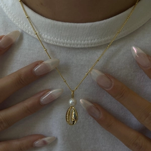 Detailed close-up of a gold shell necklace with a white pearl on a model's neck