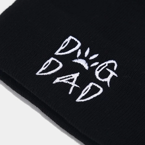 Detail der weißen DOG DAD Stickerei auf einer schwarzen Strickmütze mit feiner Textur