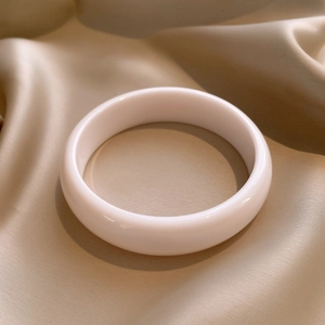 Close-up of a white resin bangle on champagne silk fabric with an elegant smooth texture