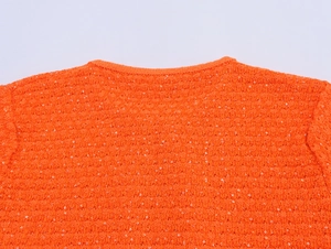 Detail des orangefarbenen Strickoberteils mit glänzenden Pailletten und Rippstrick