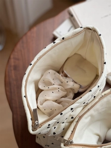 Close-up of quilted cream makeup bag with black hearts showing inner storage and zipper