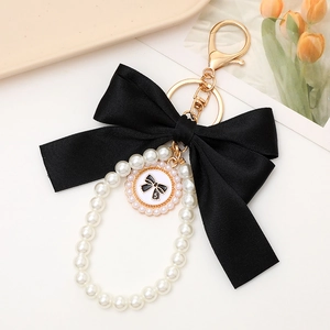 Detail of elegant black bow and pearl keychain with number 5 charm on a soft beige tray