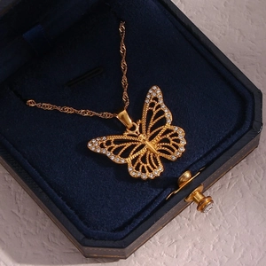 Macro view of a gold hollow butterfly pendant with white zircon on a blue velvet box