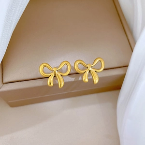 Close-up of golden bow-shaped stud earrings on a beige jewelry box with soft white fabric