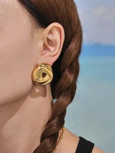 Detailed close-up of chunky gold-plated twisted knot earrings with a polished finish