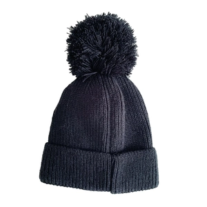 Close-up of thick black knitted texture and matching soft pom-pom on the winter beanie