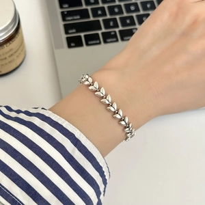 Makroaufnahme eines silbernen Weizenblatt-Armbands am Handgelenk vor Laptop-Hintergrund