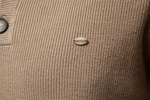 Close-up of khaki knit sweater texture showing high-quality stitching and metal brand tag
