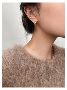Close-up of golden teardrop earring worn by a model in soft lighting detail