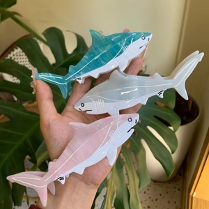 Detailed view of hand-held shark shaped hair clips in blue grey and pink acetate texture
