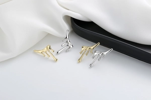 Close-up of stylish 18K gold and silver liquid lava style earrings on white silk