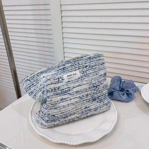 Blue and white tweed makeup bag with gold zipper and simple wish label on display