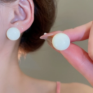 Detail view of large round cream-colored resin stud earrings on model for size scale