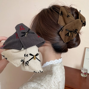 Detail of tweed bow hair clips in brown, grey and beige with gold metal pendants