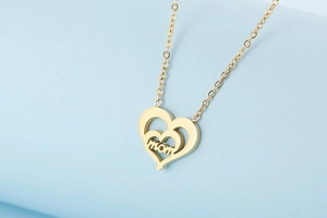 Close-up of golden double-layered heart pendant with MOM lettering on a blue pedestal