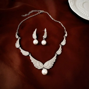 Elegant angel wing jewelry set with rhinestones and faux pearls on dark fabric