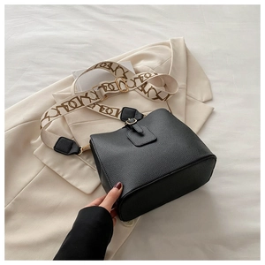 Detail of black lychee grain bucket bag with wide jacquard shoulder strap on beige blazer