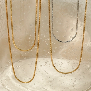 Collane a catena serpente in acciaio inossidabile oro e argento su vetro con gocce d'acqua