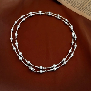 Detailed shot of double-layered silver chain necklace with pearls on a dark red fabric