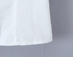Dettaglio della camicetta in cotone bianco con ricamo floreale traforato sull'orlo
