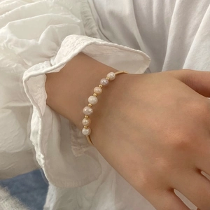 Close-up of elegant gold pearl bracelet on a model wearing white lace sleeve