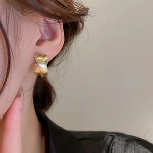 Detailed side view of a matte gold twisted X-shaped earring on a model's ear