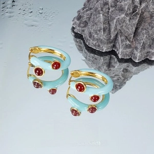 Detailed view of blue enamel earrings with red gemstones on artistic rock background
