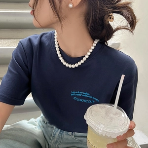 Detail of elegant pearl necklace styled with a blue slogan tee for a vintage French aesthetic