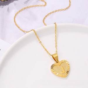 Detail of gold heart pendant with embossed letter J on textured matte finish