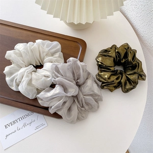 Close-up of white, grey, and olive green oversized scrunchies with metallic shimmer texture