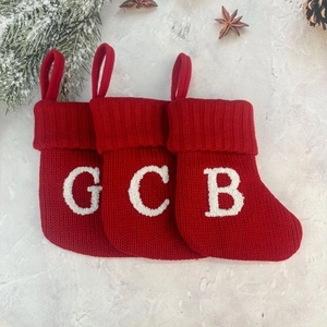 Close-up of red knitted Christmas stockings with white letters G, C, B on marble surface