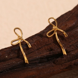 Detail of golden stainless steel bow stud earrings on natural wood stand