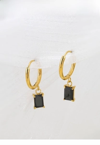 Macro shot of gold titanium earrings with rectangular black zircon charms on white fabric