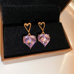 Macro shot of purple heart-shaped stone earrings in a golden frame inside a jewelry box