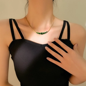 Elegant gold snake chain necklace with green gemstone worn by a model in black