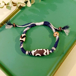 Detail of hand-woven ethnic bracelet with black and white agate dZi beads on a green tray