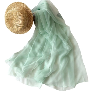 Light green chiffon sun shawl and straw hat displayed on a clean white background