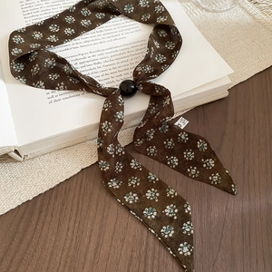 Detailed view of floral chiffon scarf necklace with black beads on a vintage book
