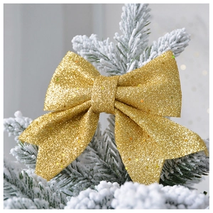 Close-up of golden glitter bow ornament on a snowy Christmas tree branch for holidays