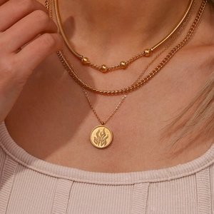 Macro detail of triple-layered gold necklaces with beads and a flame emblem pendant